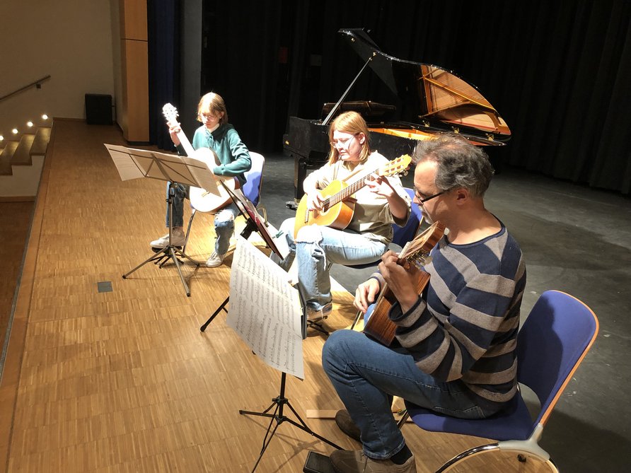 Zwei Schülerinnen mit Gitarre und ihrem Lehrer Michael Distler auf der Bühne